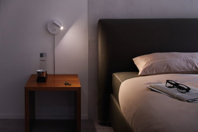 Moderner weißer LED-Wandleuchter mit schwenkbarem Spot über Nachttisch aus Holz im Schlafzimmer.