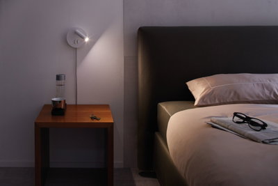 Moderne witte LED-wandlamp met verstelbare spot boven houten nachtkastje in slaapkamer.