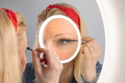 Frau trägt Wimperntusche vor beleuchtetem Kosmetikspiegel mit LED-Ring für präzises Make-up.