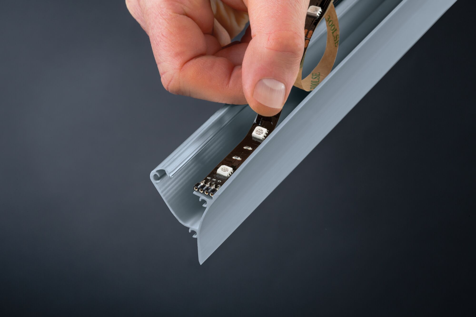 Hand inserts black LED strip into grey aluminum profile for LED lighting installation