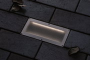Rectangular stainless steel recessed light with warm white glow in dark outdoor paving for garden lighting