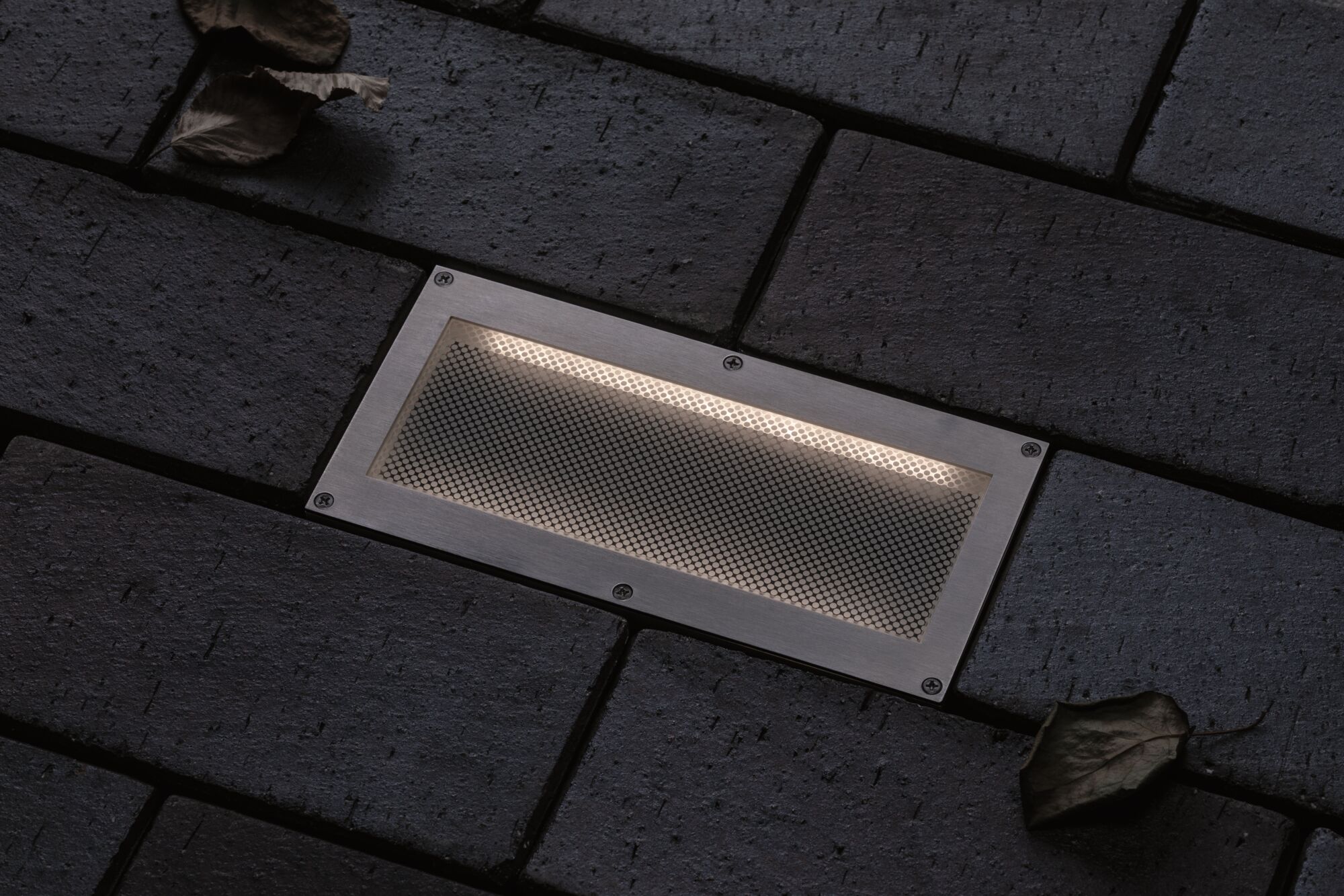 Rechthoekige inbouwlamp van roestvrij staal met warm wit licht in donkere buitenbestrating