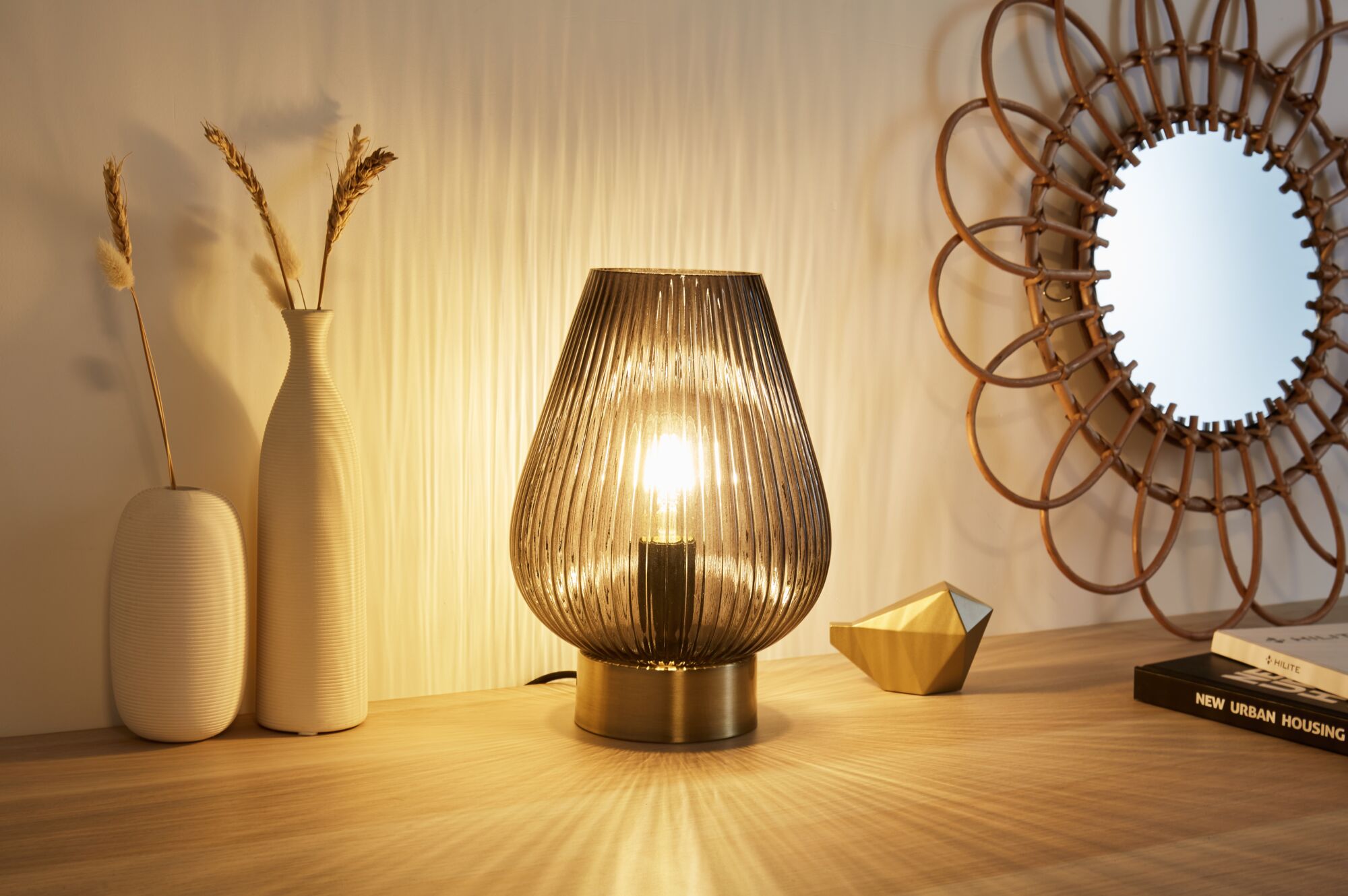 Modern brown ribbed glass table lamp with warm light on wooden surface next to decor and mirror