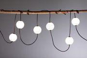 Moderne LED-Lichterkette mit weißen Kugeln an schwarzem Kabel, dekorativ an Holzast hängend