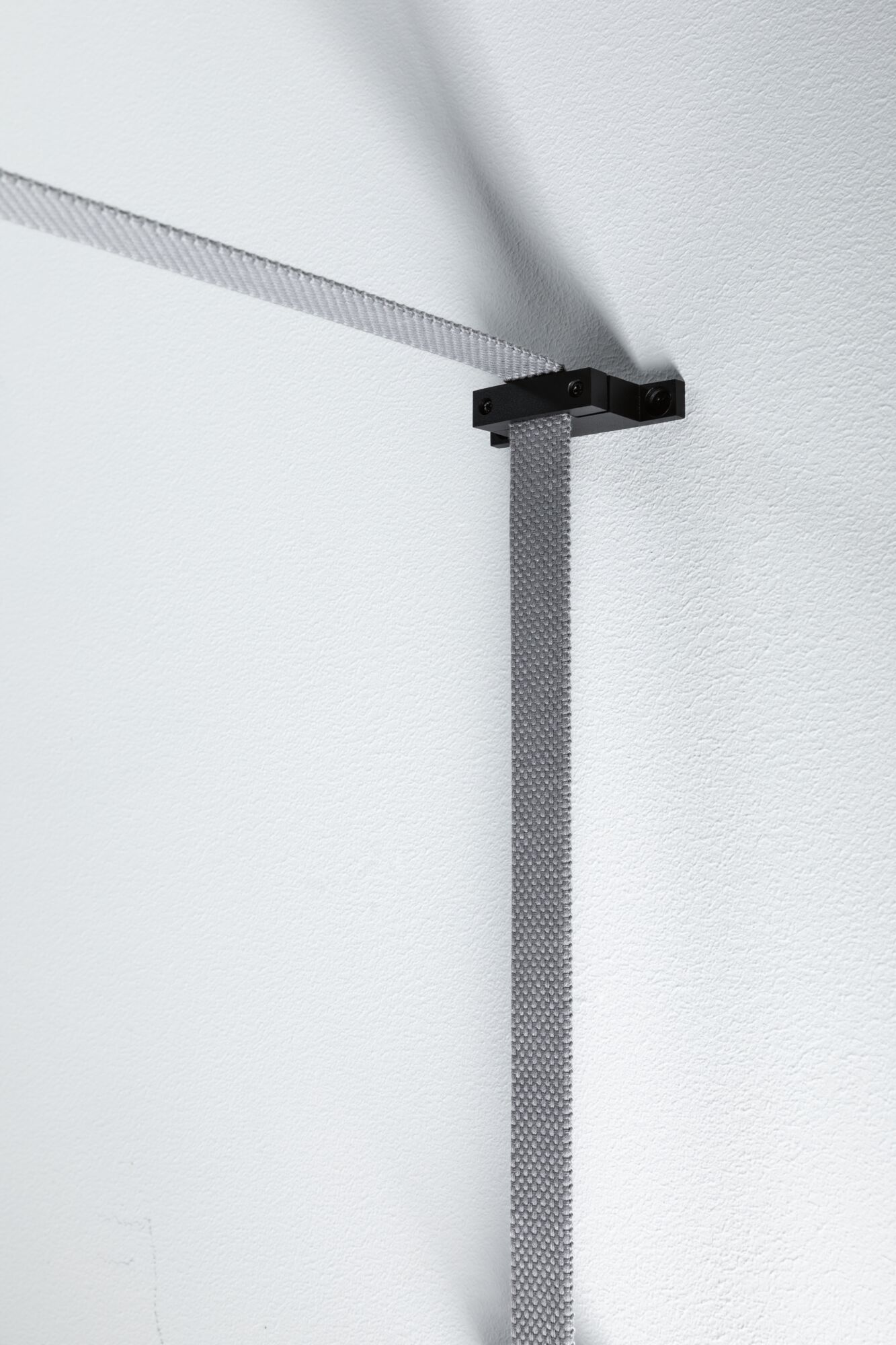 Grauer textiler Kabelhalter aus Metall an weißer Wand für moderne Beleuchtungssysteme