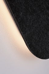Close-up of black felt wall lamp with warm white LED light on white wall for modern lighting