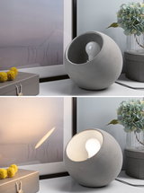 Round table lamp made of grey concrete with visible bulb, modern home accessory for ambient lighting