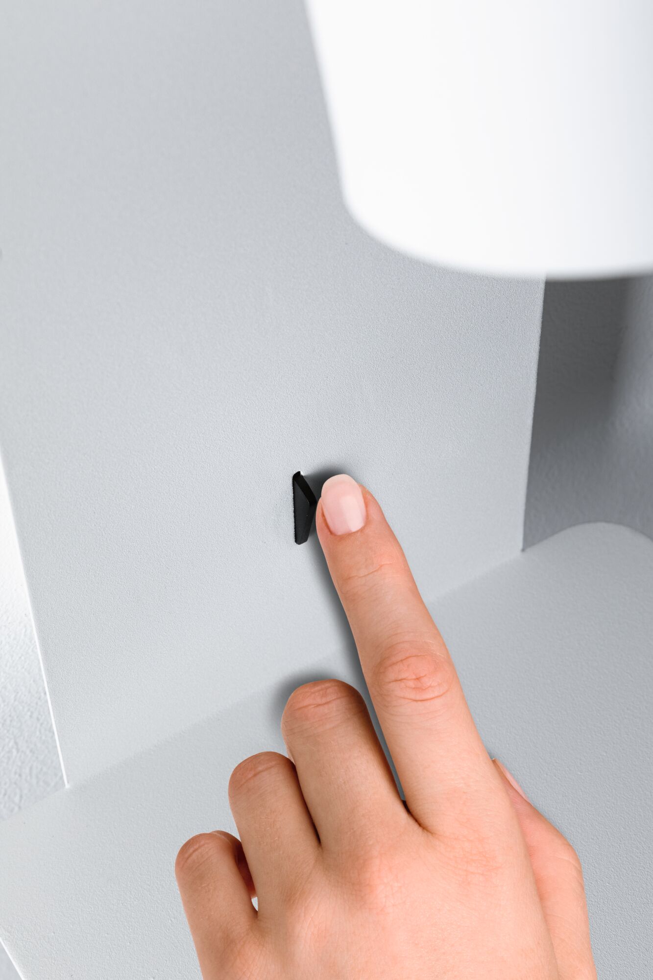 Hand pressing small black switch on white-grey metal wall lamp for home lighting
