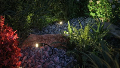 Trois projecteurs LED noirs sur gravier éclairant des plantes pour éclairage extérieur et jardin.