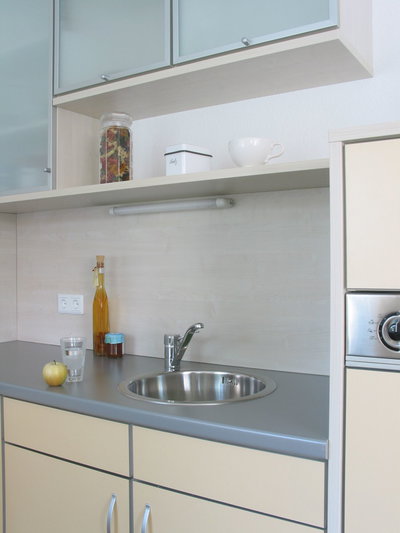 Modern kitchen with stainless steel sink, grey countertop and light cabinet fronts for kitchen lighting.