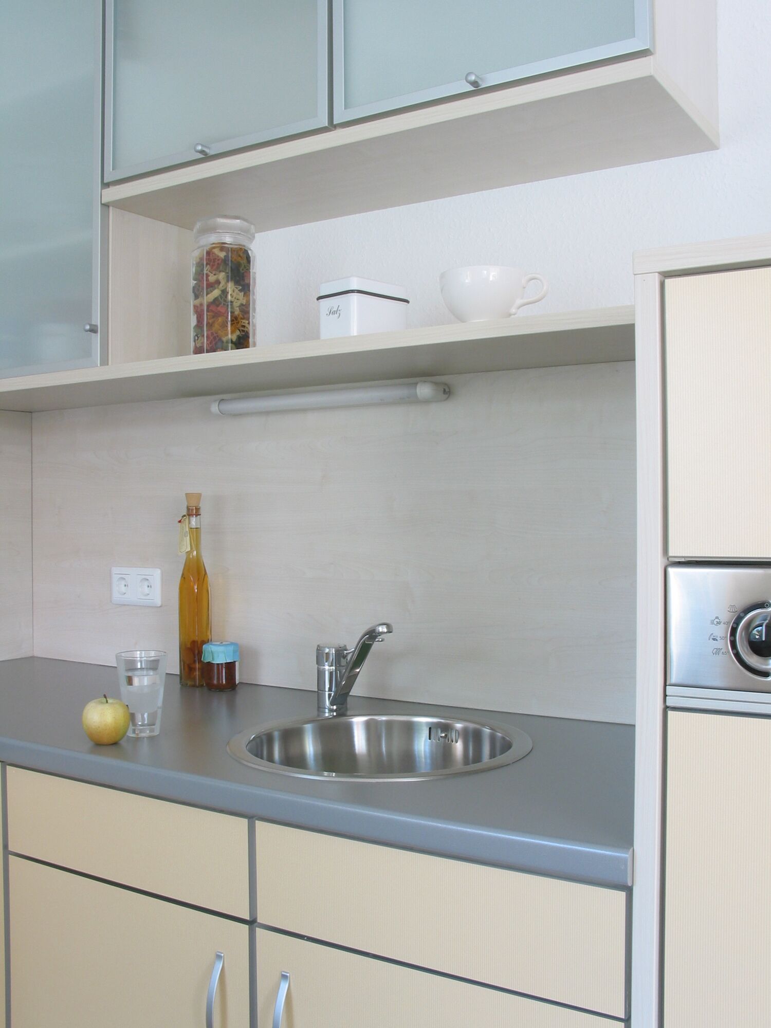 Cuisine moderne avec évier en acier inoxydable, plan de travail gris et façades claires pour éclairage cuisine.