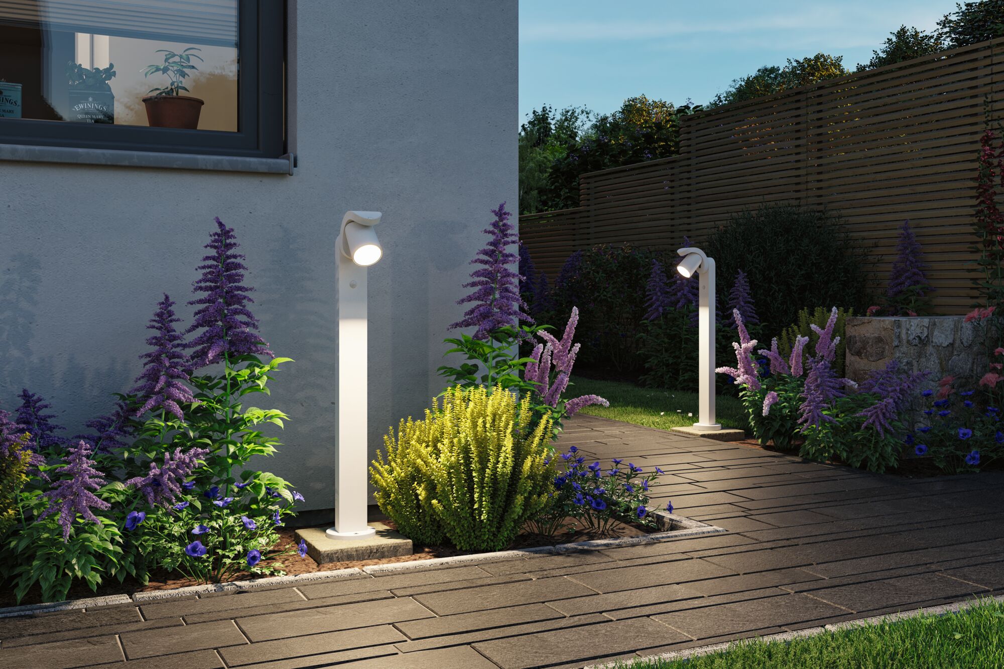 Weiße moderne Außenwandleuchten aus Metall beleuchten Gartenweg mit bunten Blumen und Sträuchern.