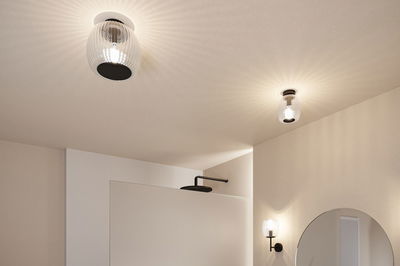 Luminaires de plafond et muraux modernes en verre cannelé et métal noir dans une salle de bain lumineuse.