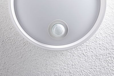 Round white ceiling light with integrated motion sensor on textured wall for indoor lighting