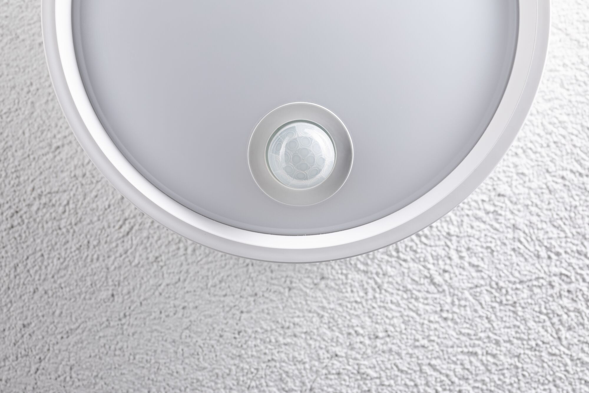 Round white ceiling light with built-in motion sensor on textured wall surface