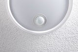Round white ceiling light with built-in motion sensor on textured wall surface