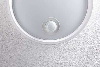 Runde weiße Deckenleuchte mit integriertem Bewegungsmelder an strukturierter Wand