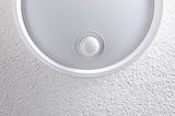 Round white ceiling light with integrated motion sensor on textured wall for indoor lighting
