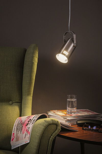 Moderner silberner LED-Hängeleuchte aus Metall über grünem Sessel und Holztisch mit Glas und Zeitschriften