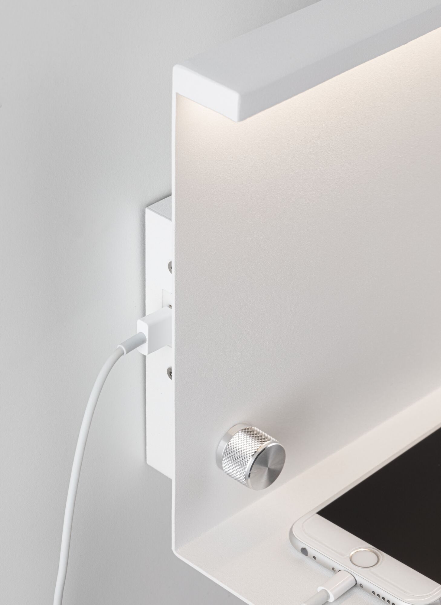 Applique murale blanche moderne avec bouton rotatif en aluminium et port de charge USB près d’un smartphone.
