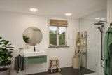 Modern bathroom with green vanity cabinet, round mirror, and black shower fixtures in bright setting