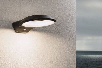 Black aluminium wall light with warm white LED ring and motion sensor on exterior wall by the sea