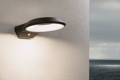 Applique murale noire en aluminium avec anneau LED blanc chaud et détecteur de mouvement sur mur extérieur face à la mer