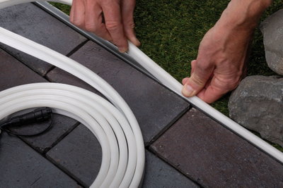 Weiße flexible LED-Lichtleiste wird zwischen Pflastersteinen und Rasen verlegt für Gartenbeleuchtung