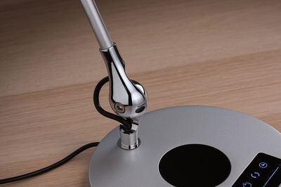 Gros plan d’un pied de lampe argenté avec articulation chromée et câble noir sur surface en bois