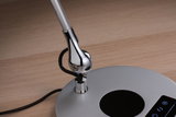 Gros plan d’un pied de lampe argenté avec articulation chromée et câble noir sur surface en bois