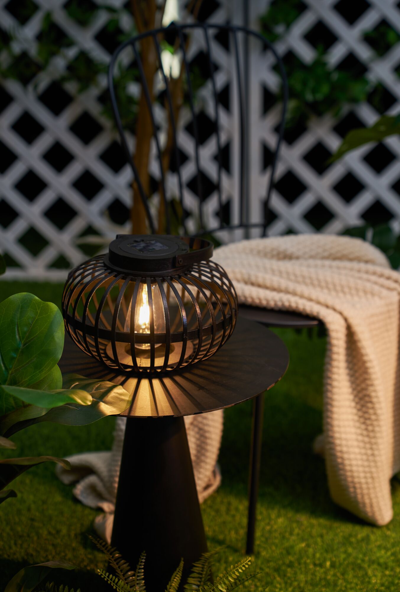 Schwarze Metalllaterne mit warmem Licht auf Tisch im Garten, dekorative Outdoor-Beleuchtung für Terrasse