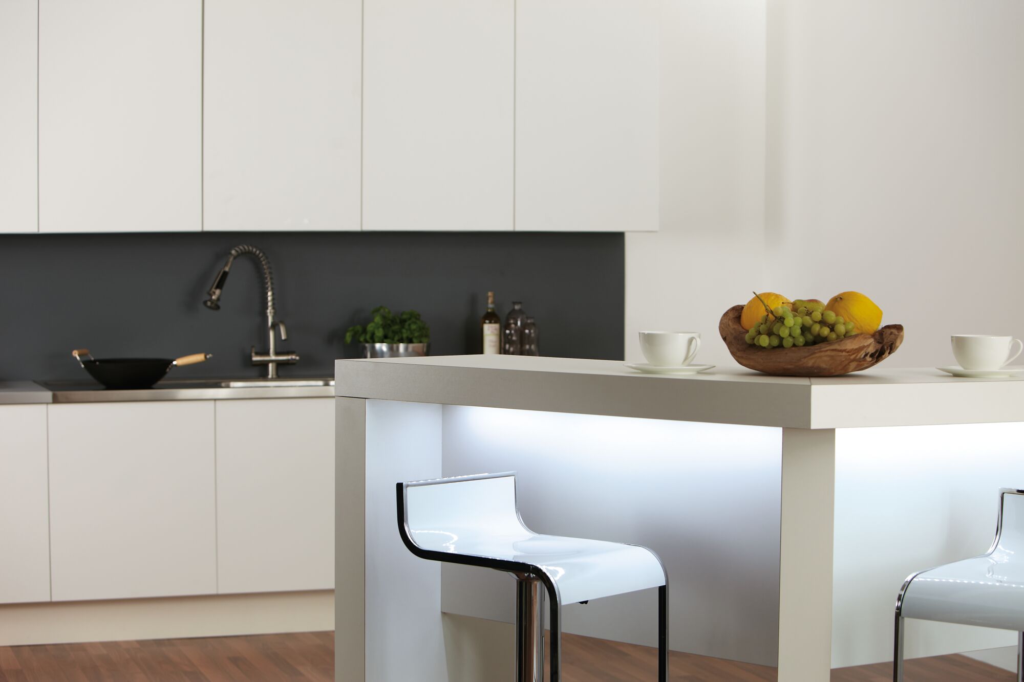 Modern white kitchen island with LED lighting and two white plastic and metal bar stools
