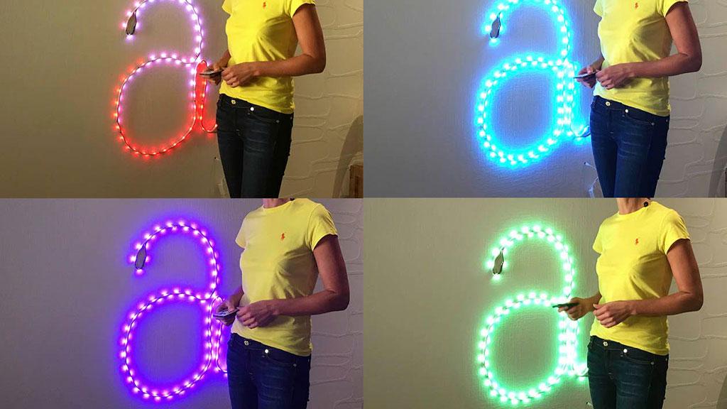 Woman controls colorful LED wall light shaped as large letter a using remote control.