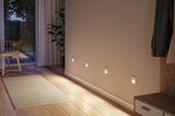 Four white LED wall lights on beige wall with wooden floor and rug in modern hallway.
