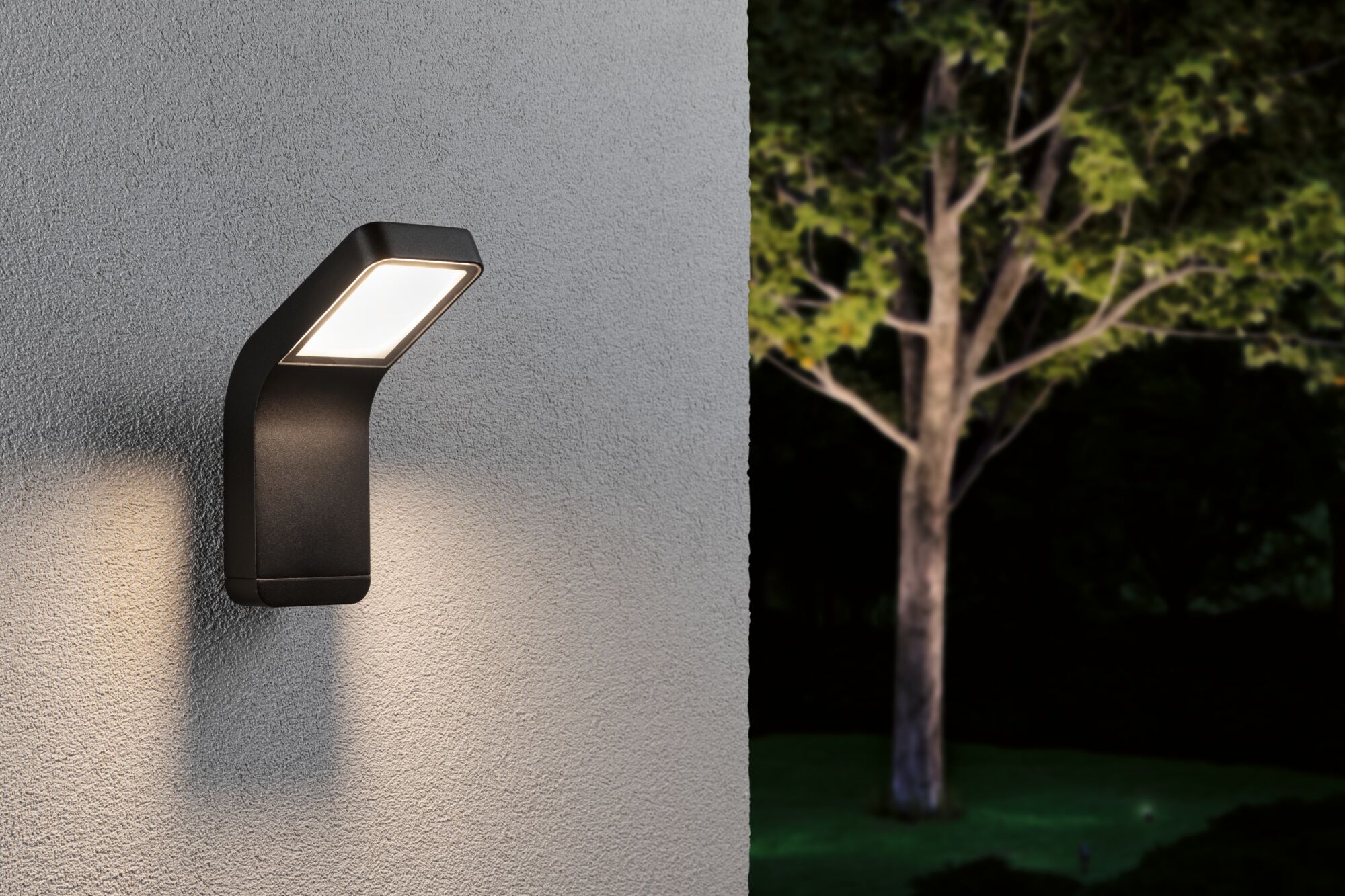 Schwarze LED-Außenwandleuchte aus Metall mit warmweißem Licht an grauer Wand im Garten.
