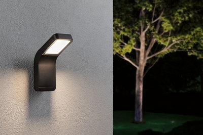 Black metal LED outdoor wall light with warm white illumination on grey wall in garden.