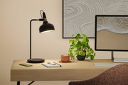 Black metal desk lamp with adjustable head on light wood desk in office workspace