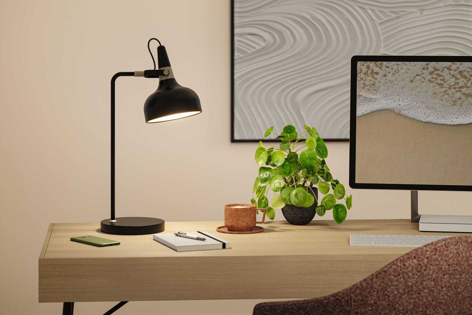 Black metal desk lamp with adjustable head on light wood desk in office workspace