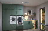 Moderne grüne Einbauküche mit Waschmaschine, Trockner und Wäschekorb in hellem Hauswirtschaftsraum