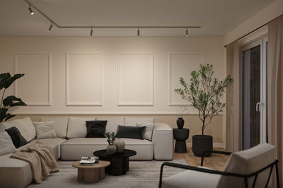 Moderne woonkamer met beige bank, zwarte en grijze kussens, houten en zwarte salontafels, planten en plafondspots