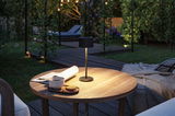 Black metal LED table lamp on wooden garden table with cup and cookies in evening light