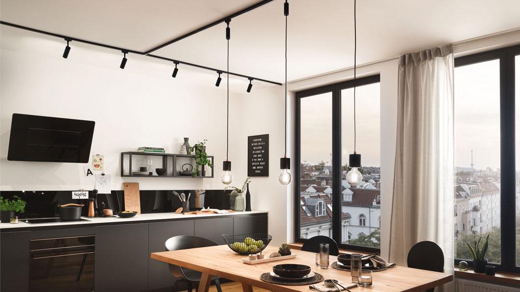 Modernes Esszimmer mit schwarzer LED-Schienenbeleuchtung und drei hängenden Glühbirnen über Holztisch.
