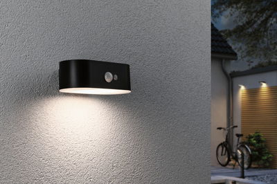 Black metal outdoor wall light with motion sensor and warm white light for home facades.
