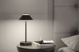 Modern black leather table lamp on round bedside table next to grey upholstered bed for bedroom lighting