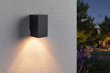 Zwarte metalen buitenwandlamp met warm wit licht op gestructureerde muur in tuin bij schemering
