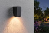 Black metal outdoor wall light with warm white illumination on textured wall in garden at dusk