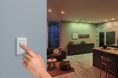 Main actionnant un interrupteur mural blanc pour éclairage LED intelligent dans un salon moderne.