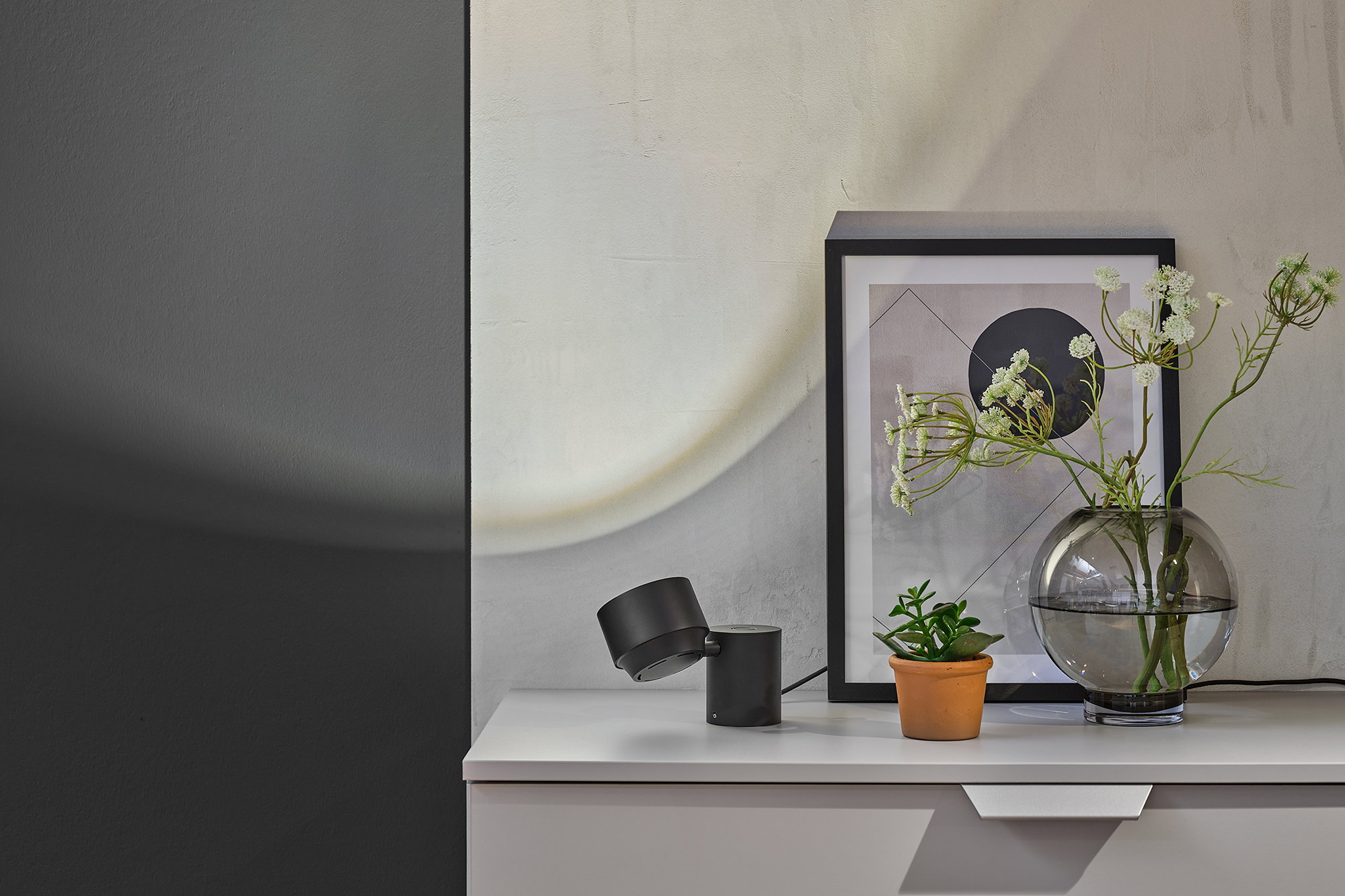 Lampe de table LED noire en métal à côté de plantes et d'une œuvre d'art moderne sur un buffet blanc