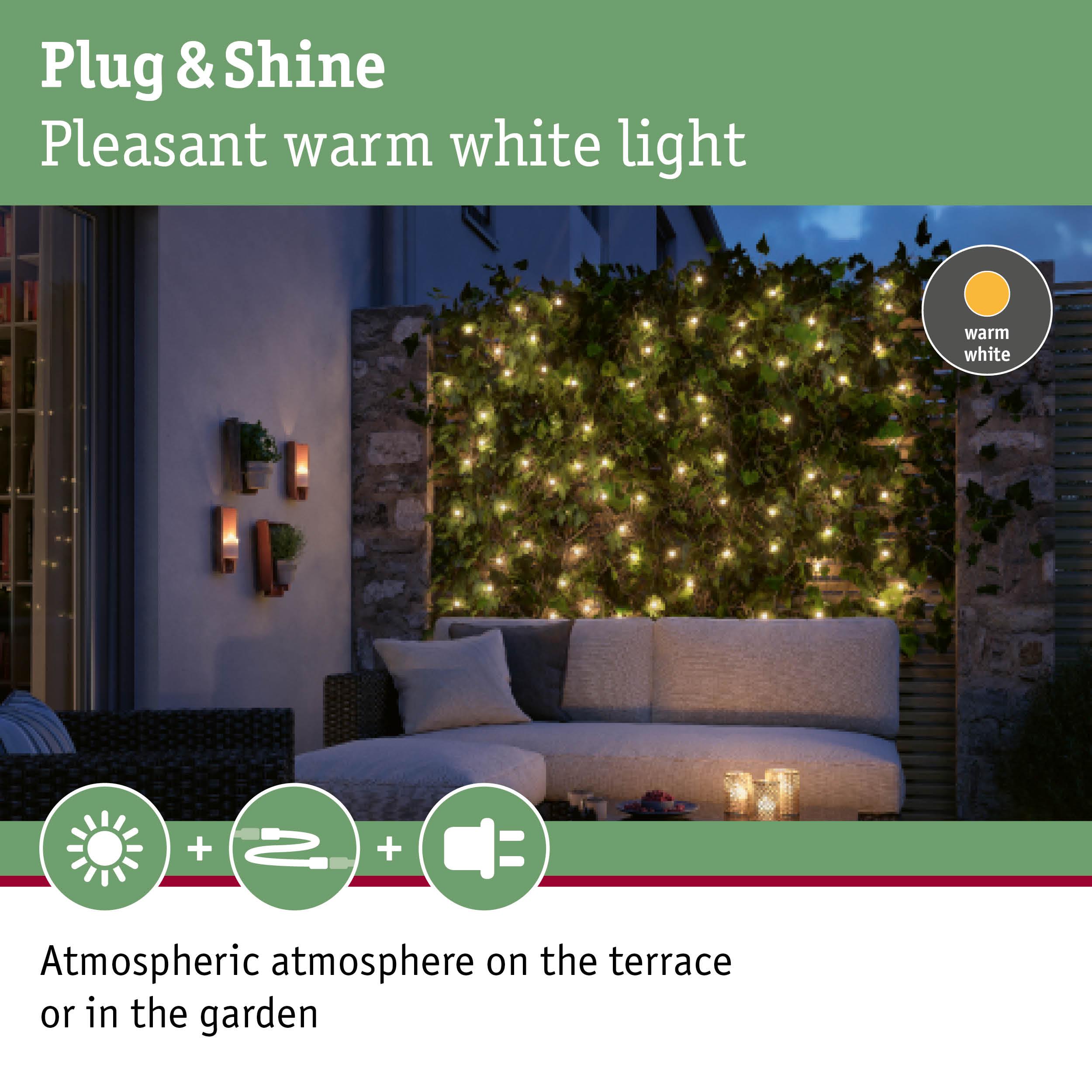 Cozy terrace with warm white LED string lights on green hedge creating atmospheric garden lighting