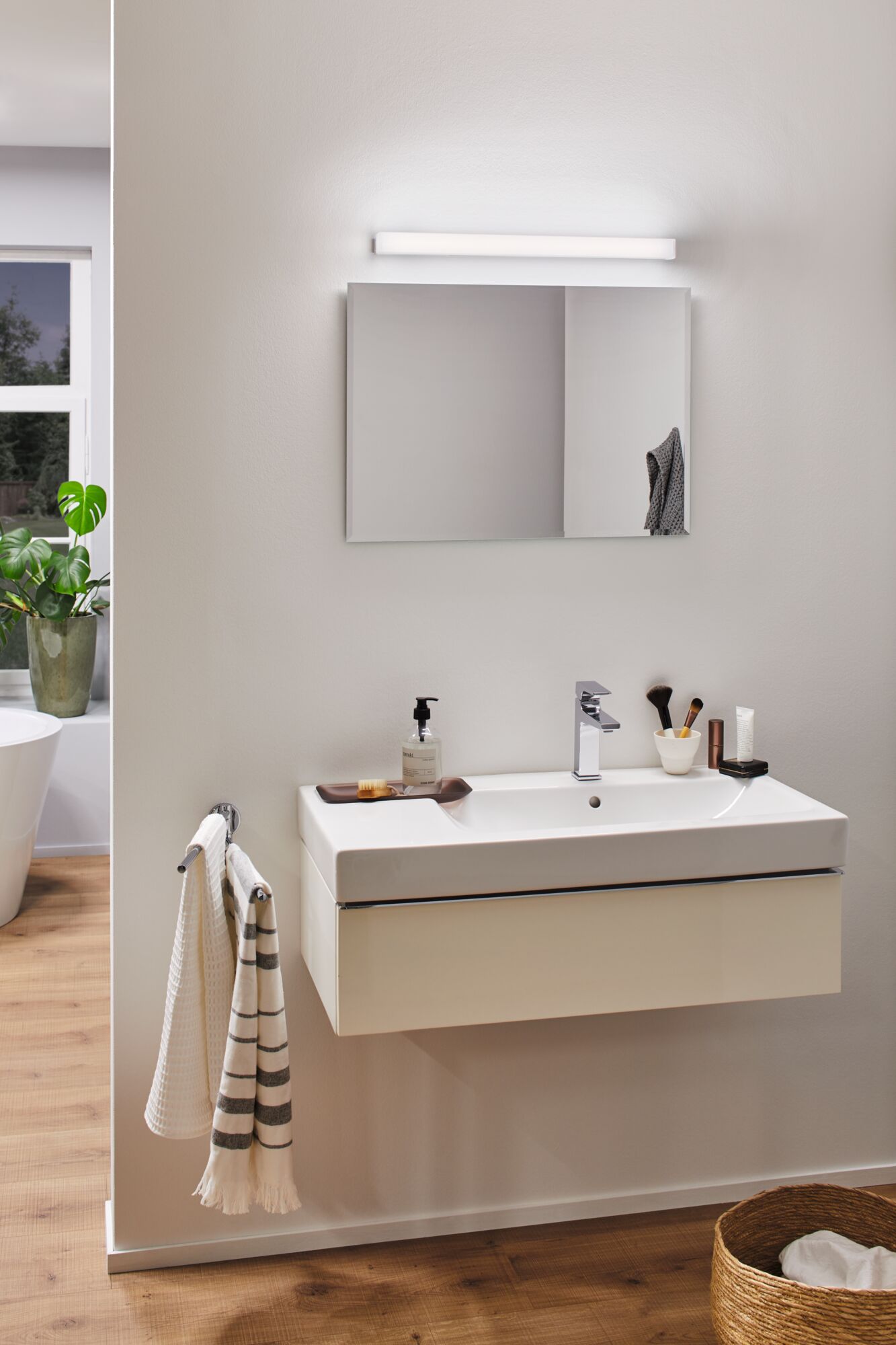 Modernes Badezimmer mit weißem Wandwaschbecken, verchromtem Wasserhahn und LED-Spiegelleuchte
